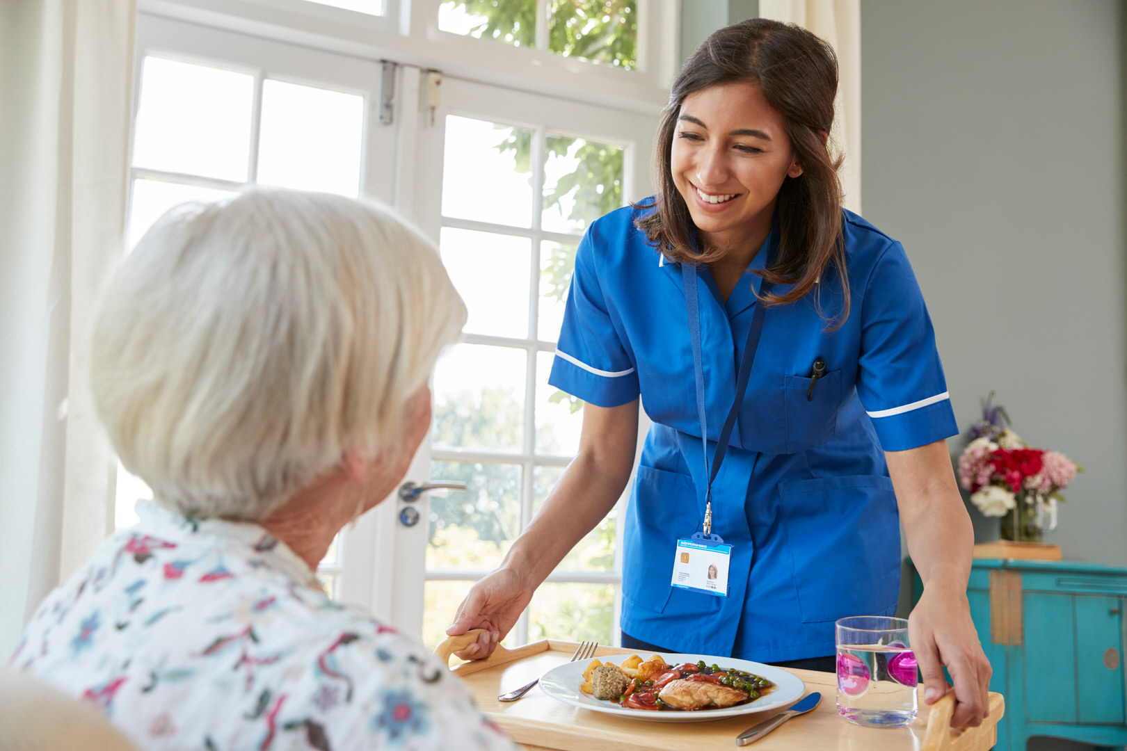 Care nurse serving dinner to a senior woman at home